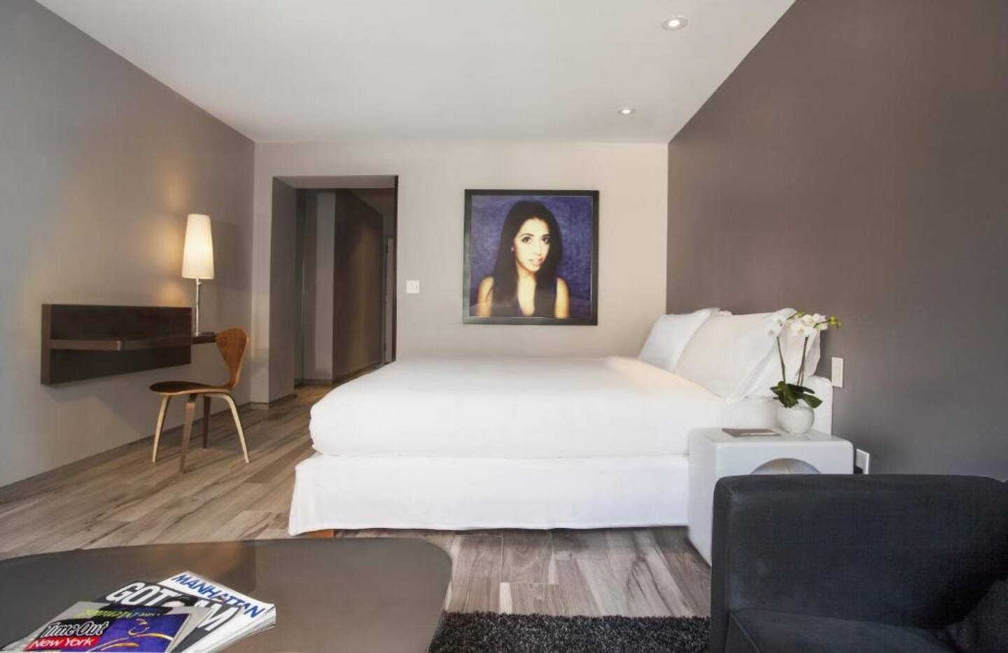 A wide view of a hotel room with a king-sized bed, a chair, a desk, and a painting on the wall.