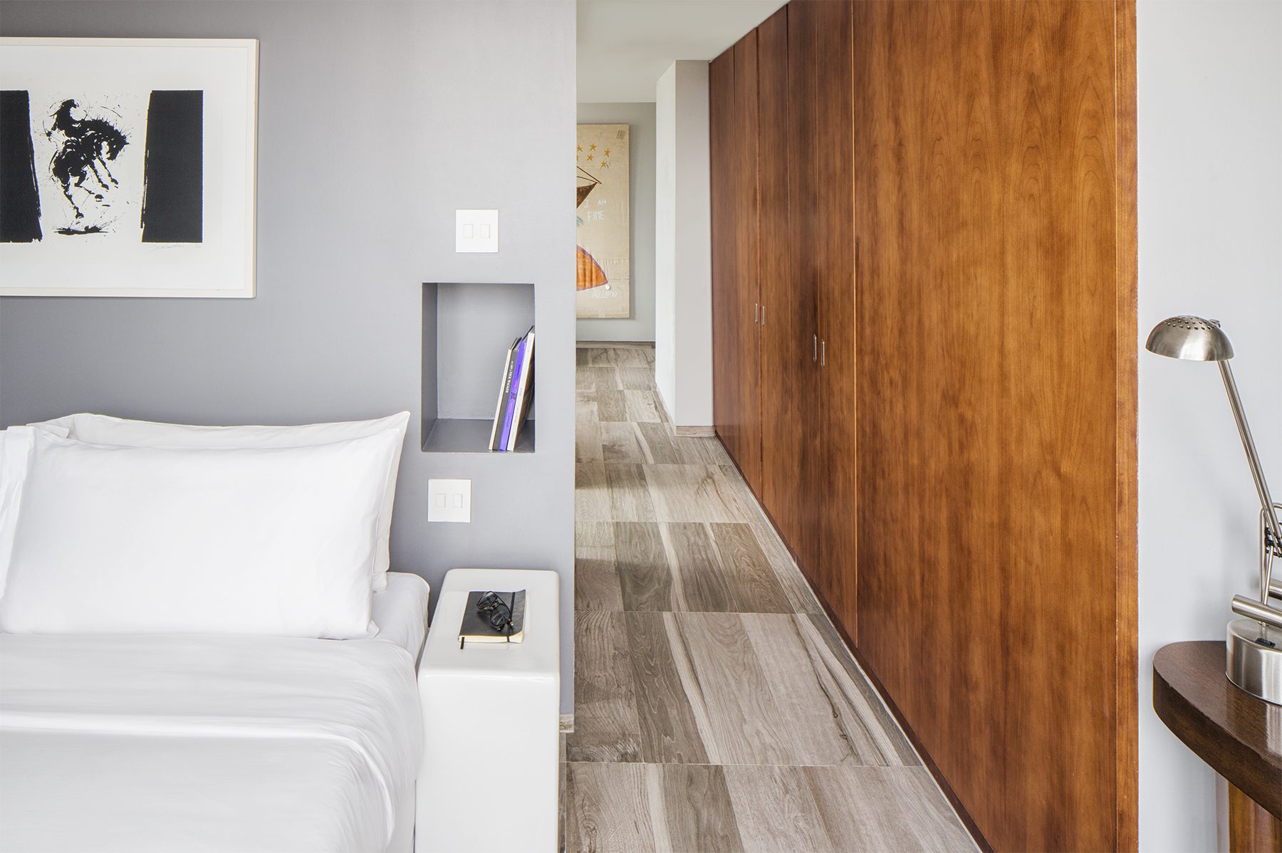 A modern hotel room with a white bed, wood paneling, and gray walls.